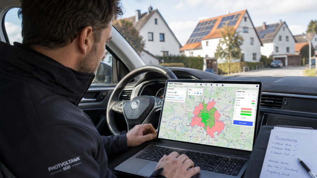 Photovoltaik-Vertriebsmitarbeiter plant im Auto Verkaufsgebiete mit einer farbigen PLZ-Karte auf dem Laptop